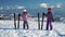 Little girls in outwear and helmets posing with skis on snow with mountain range on background