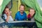 Little girls sisters and brother boy sitting inside green camp tent drinking tea and cheerfully laughing and looking into camera.