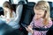 Little girls, sisters are driving in car, children play video games in tablet and mobile phone. Traveling on road in safe baby