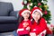 Little girls sitting with her friend and smiles in front of Christmas tree