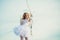 Little goddess with white wings alone on blue sky background. Portrait of little curly blond Angel girl. Girl angel with