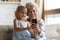 Little granddaughter aged grandmother having fun at home using smartphone