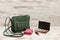 Little green ladies handbag, pink purse, eyeshadow palette and lipstick on wooden background. fashion concept