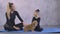 Little gymnastic asian girl in black bodysuit with trainer sitting on yoga mat and stroking small ginger chihuahua dog