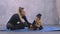 Little gymnastic asian girl in black bodysuit with trainer sitting on yoga mat and stroking small ginger chihuahua dog