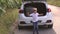 Little happy boy jumps next to the trunk of the car in which the suitcase lies