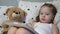 Little happy child plays a tablet while lying on a bed with a teddy bear. The kid watches the children`s channel through