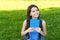 Little happy girl reading book outdoors sunny day, daydreamer concept