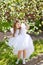 A little happy girl in a white dress is dancing under a blooming apple tree with flowers. Summer entertainment for families with