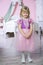 Little happy princess girl in pink dress and crown in her royal room posing and smiling.