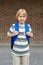 Little happy schoolboy at school yard, carrying backpack. Back to school concept. Student against brick wall