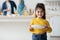 Little Helper. Cute Arab Girl Holding Plates In Kitchen, Smiling At Camera