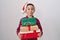 Little hispanic boy wearing christmas hat holding presents puffing cheeks with funny face