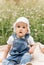 A little infante girl in a white cap sits in the park among the flowers