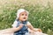 A little infante girl in a white cap sits in the park among the flowers