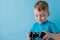 Little kid boy 2-3 years old wearing blue clothes hold in hand joystick for gameson blue background children studio portrait.