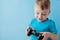 Little kid boy 2-3 years old wearing blue clothes hold in hand joystick for gameson blue background children studio portrait.