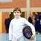 Little kid boy fencing on a fence competition. Child in white fencer uniform with mask and sabre. Active kid training