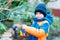 Little kid boy hanging bird house on tree for feeding in winter