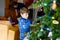 Little kid boy and his dad taking down holiday decorations from Christmas tree. Father on background. Family after