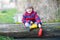 Little kid boy playing with paper ship by puddle