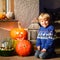 Little kid boy sitting with traditional jack-o-lanterns pumpkins for halloween by the decorated scary door, outdoors