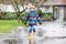 Little kid boy wearing yellow rain boots and walking during sleet, rain and snow on cold day