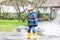 Little kid boy wearing yellow rain boots and walking during sleet, rain and snow on cold day. Child in colorful fashion