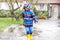 Little kid boy wearing yellow rain boots and walking during sleet, rain and snow on cold day. Child in colorful fashion