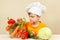 Little kid in chefs hat chooses vegetables for salad at table