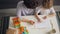 Little kid drawing and colouring picture with careful mother at table at home