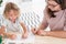 Little kid drawing a house using colorful crayons with his female, therapist during a meeting in the office