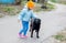 A little kid girl in a blue jacket and hat stroking the back of a black large stray dog in the yard