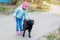 A little kid girl in a blue jacket and pink hat stroking the head of a black large stray dog in the yard