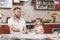 Little kid girl helps man to cook Christmas ginger cookies, playing, sprinkling flour at table. Happy family dad, child