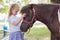 Little kid girl holding cuddling her pony horse outdoors outside green park background