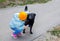 A little kid girl in a light blue jacket and hat stroking the back of a black large stray dog in the yard