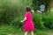 Little kid girl with pigtails in a pink summer dress launches huge soap bubbles in the garden. back view