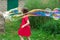 Little kid girl with pigtails in a red summer dress launches huge soap bubbles in the garden