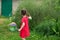 Little kid girl with pigtails in a red summer dress launches huge soap bubbles in the garden