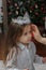 Little kid girl with tiara on head with christmas tree on background