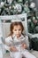 Little kid girl with tiara on head with christmas tree on background