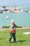 Little kid in jacket and hat smiling and spreading his hands on background of sea bay in spring