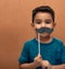 Little kid joking with a fake paper moustache. Happy child playing in home. wooden Isolated background. Movember concept