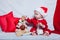 A little kid in a red cap eats a cookies and milk. Christmas photography of a baby in a red cap. New Year holidays and Christmas