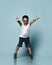 Little kid in sunglasses, white t-shirt, denim shorts and khaki sneakers. Scaring you, raised his hands, posing on blue background