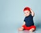 Little kid in t-shirt, red shorts and cap, barefoot. He holding a rattle, sitting on floor against blue background. Close up