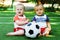 Little kids in uniform learning to play with soccer ball at sports ground. Little boy and blonde girl playing with football ball