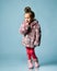 Little lady dressed in pink faux fur coat, pants and boots. She smiling, gesticulating, posing on blue background. Full length