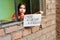 Little latin girl standing near the window and holding a sheet of paper that says in spanish `When will I go back to school?`.